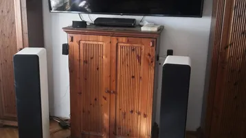 Wohnzimmer mit großem Fernseher, Soundsystem und traditionellen Holzschränken, durchflutet von Sonnenlicht.