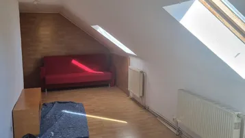 Helles Dachzimmer mit schrägen Wänden, Dachfenstern, rotem Sofa und Laminatboden, derzeit in Renovierung.