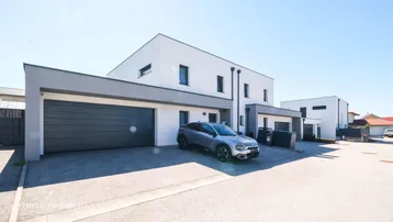 Moderne Doppelhaushälfte mit integrierter Garage und Stellplatz im Freien.