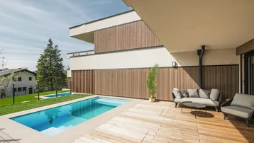 Geräumige Holzterrasse mit privatem Pool und gemütlicher Lounge-Sitzgruppe unter blauem Himmel.