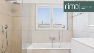 Modernes Badezimmer mit Badewanne, Regendusche und Fenster, hell gefliest und mit Logo.