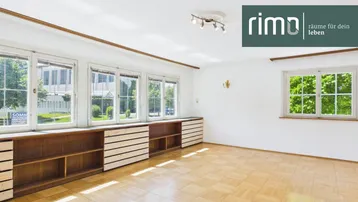 Helles Wohnzimmer mit Parkettboden, großen Fenstern und eingebauten Regalen.