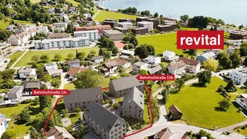 Luftaufnahme der modernen Wohnanlage am Seeufer mit umliegender Natur und Bergen im Hintergrund.