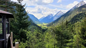 Malerischer Blick auf ein grünes Tal und schneebedeckte Berge unter bewölktem Himmel.