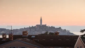 Panoramablick auf eine Küstenstadt mit Kirchturm bei Sonnenuntergang und Dächern im Vordergrund.