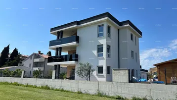 Modernes Mehrfamilienhaus mit weißer Fassade, schwarzen Akzenten und Balkonen unter blauem Himmel.