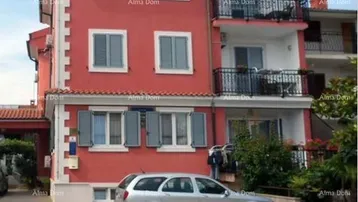 Rotes Mehrfamilienhaus mit mehreren Balkonen und einem geparkten Auto davor.