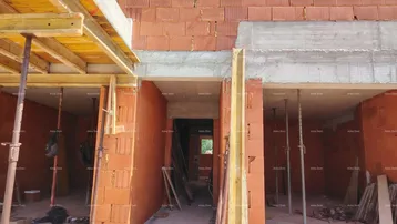 Fassade eines im Bau befindlichen Gebäudes mit sichtbaren Ziegelwänden und Betonelementen.