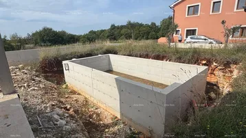 Baustelle mit Rohbau eines Pools und umliegendem, noch unfertigem Gelände unter blauem Himmel.