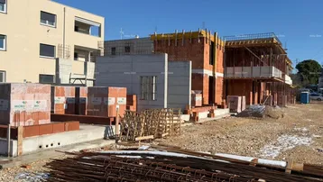 Baustelle mit im Bau befindlichen Gebäuden und Baumaterialien unter blauem Himmel.