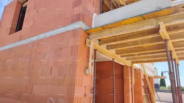 Rohbau eines Gebäudes mit roten Ziegelwänden und Holzschalung im Bau.