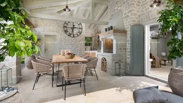 Gemütliche überdachte Terrasse mit Essbereich und integriertem Außenkamin, umgeben von Steinmauern.
