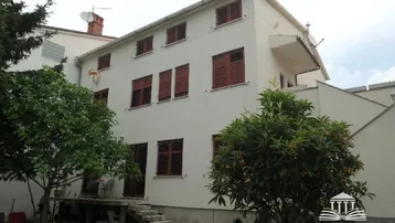 Weißes Mehrfamilienhaus mit braunen Fensterläden und einem kleinen Gartenbereich im Vordergrund.