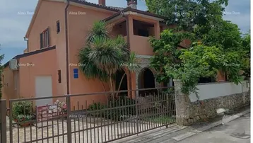Ein charmantes Haus mit orangefarbener Fassade, umgeben von mediterraner Vegetation und einem Metallzaun.