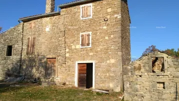 Altes Steinhaus mit rustikalen Holzfensterläden und angrenzender Ruine unter blauem Himmel.