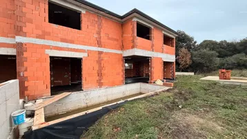 Rohbau eines Hauses mit unverputzten Ziegelwänden und vorbereitetem Fundamentbereich.
