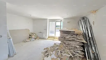 Innenraum im Rohbauzustand mit Bauschutt und Zugang zu einem Balkon.