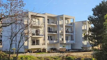 Modernes Mehrfamilienhaus mit mehreren Balkonen und großen Fenstern unter blauem Himmel.