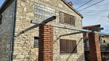 Steinfassade eines traditionellen Hauses mit Holzfensterläden und Glasbausteinen.