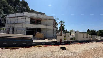 Baustelle eines modernen Hauses mit Gerüst und beginnender Fassadenverkleidung unter blauem Himmel.