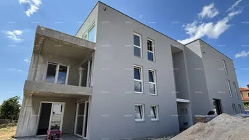 Moderne Fassade eines im Bau befindlichen Gebäudes mit grauer Putzfassade und weißen Fenstern unter blauem Himmel.