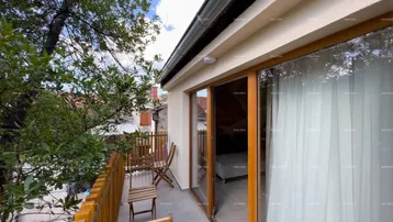 Gemütlicher Balkon mit Holzzaun und Sitzgelegenheiten, umgeben von grünen Bäumen und blauem Himmel.