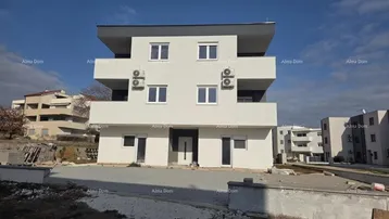 Modernes, weißes Mehrfamilienhaus mit mehreren Etagen und Balkonen, umgeben von einer Baustelle.