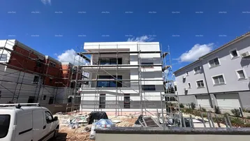 Neubauwohnung im Bau mit Gerüst an der Fassade und Baufahrzeug im Vordergrund.