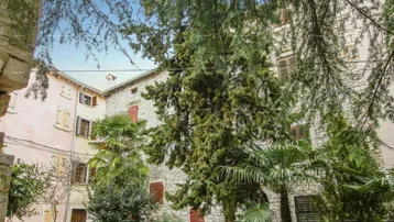 Historische Steinfassaden mit traditionellen Fensterläden und üppiger mediterraner Vegetation in einem charmanten Innenhof.