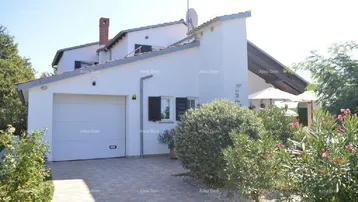 Weißes Einfamilienhaus mit Garage, gepflasterter Auffahrt und grüner Bepflanzung im Vorgarten.