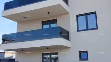 Modernes Mehrfamilienhaus mit mehreren Balkonen und Glasgeländern unter blauem Himmel.