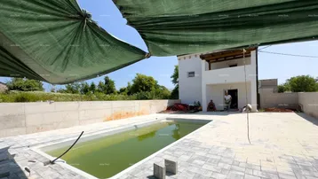 Außenbereich mit Pool in Bau, gepflasterter Fläche und einem Gebäude im Hintergrund unter blauem Himmel.