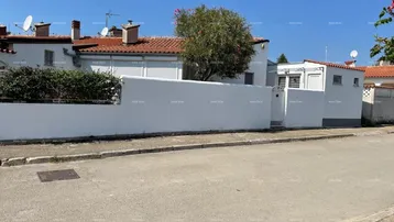 Weißes Haus mit rotem Ziegeldach und einer hohen Mauer zur Straße hin.