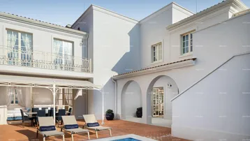 Geräumige Außenterrasse mit Pool, Sonnenliegen und Essbereich unter einer Pergola.