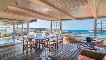Geräumige Dachterrasse mit Holzboden, Essbereich und weitem Meerblick unter einer Pergola.