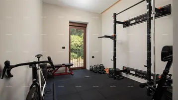 Gut ausgestatteter Fitnessraum mit Sportgeräten, Gummiboden und einem Fenster mit französischem Balkon.
