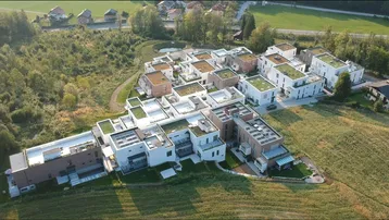 Luftaufnahme einer modernen Wohnanlage mit mehreren Gebäuden, begrünten Dächern und Terrassen in ländlicher Umgebung.