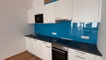 Moderne Einbauküche mit weißen Schränken, dunkler Arbeitsplatte und blauer Rückwand.
