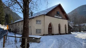 Historisches Gebäude mit markanten Rundbögen und Holzelementen, umgeben von Schnee und Bergen.