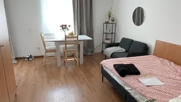 Heller Wohn- und Schlafbereich mit Holzboden, Esstisch und natürlichem Lichteinfall.