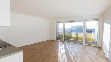 Heller offener Wohnbereich mit Parkettboden, großen Fenstern und Zugang zum Balkon.
