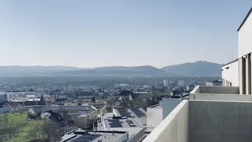 Weitläufiger Blick über die Stadt und die umliegende Landschaft mit Hügeln und einem Schloss in der Ferne.