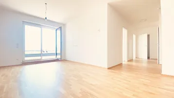 Helles, leeres Wohnzimmer mit Holzboden und Zugang zu einem Balkon oder einer Terrasse.