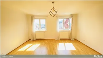 Helles Wohnzimmer mit Holzboden, zwei Fenstern und moderner Deckenleuchte, durchflutet von Sonnenlicht.