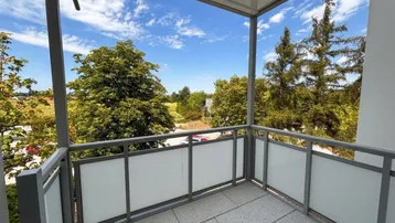 Heller Balkon mit Fliesenboden und Blick ins Grüne, umgeben von Bäumen und Natur.