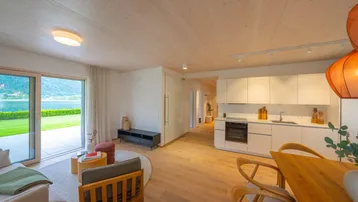 Offener Wohnbereich mit integrierter Küche, Holzboden und Zugang zur Terrasse mit Seeblick.