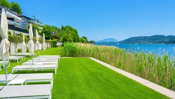 Große grüne Liegewiese mit Sonnenliegen und Schirmen am Seeufer mit Bergblick.