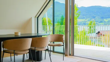 Heller Essbereich mit modernem Tisch und Stühlen, großen Fenstern, Dachschräge und beeindruckendem Seeblick.