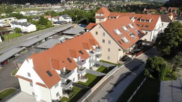 Luftaufnahme eines modernen Wohnkomplexes mit roten Dächern und Balkonen in einer bergigen Landschaft.