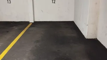 Tiefgaragenstellplatz mit weißen Wänden, dunklem Boden und Beton-Decke.